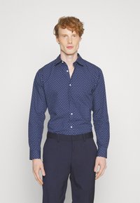 Camicia button-up blu navy con pois bianchi, maniche lunghe e colletto a punta, abbinata a pantaloni navy. Tessuto a trama liscia.