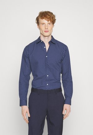 Camicia button-up blu navy con pois bianchi, maniche lunghe e colletto a punta, abbinata a pantaloni navy. Tessuto a trama liscia.