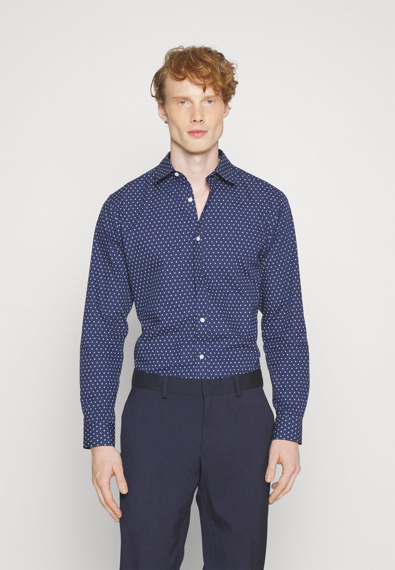 Camicia button-up blu navy con pois bianchi, maniche lunghe e colletto a punta, abbinata a pantaloni navy. Tessuto a trama liscia.