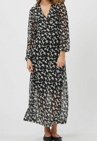 Robe longue à manches longues en noir et blanc avec un voile transparent et un motif abstrait. Elle présente un décolleté en V et une silhouette fluide.