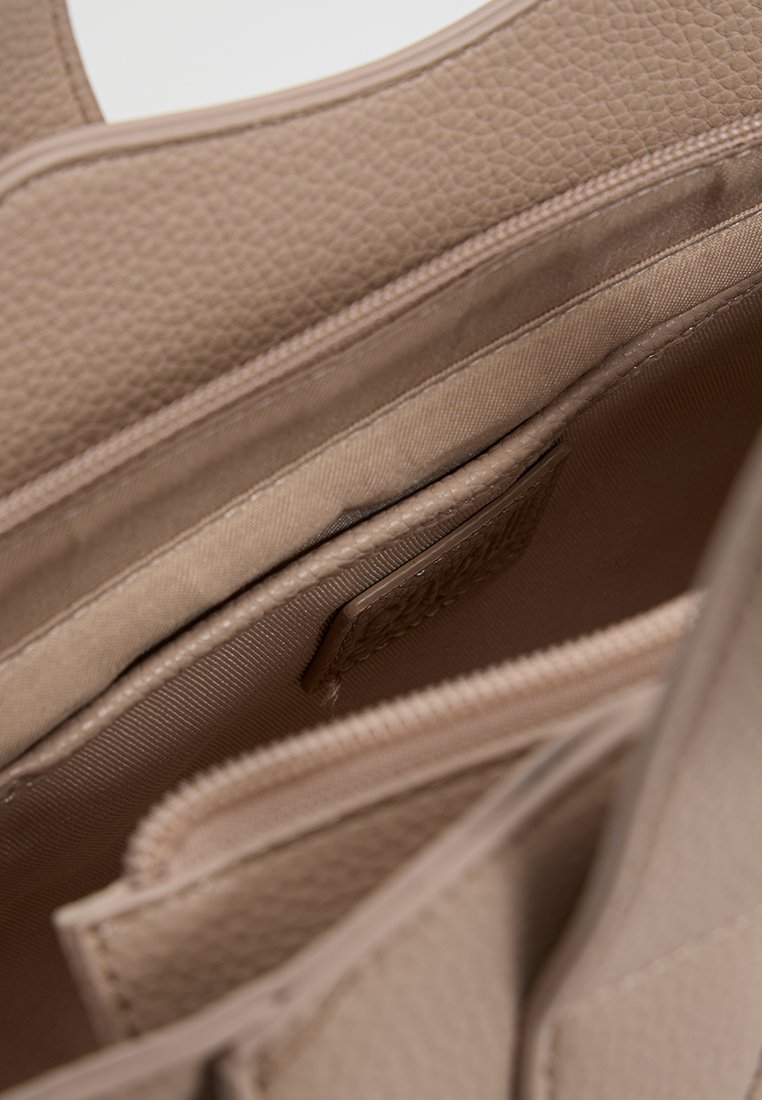 Interior de bolso texturizado beige con múltiples compartimentos. Cuenta con un forro suave y un cierre de cremallera. Diseño suave y estructurado en toda su extensión.