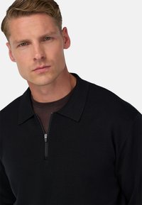 Črna zip majica s polo ovratnikom, teksturirana tkanina in notranja rjava plast vidna na ovratniku. Prilagojena zasnova.
