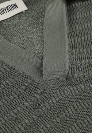 Grüner Strickpullover mit V-Ausschnitt und strukturiertem Muster; Drykorn-Markenlabel ist am Krageninneren sichtbar.