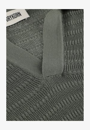 Grüner Strickpullover mit V-Ausschnitt und strukturiertem Muster; Drykorn-Markenlabel ist am Krageninneren sichtbar.