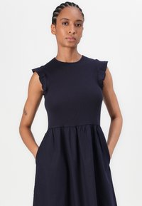 Dunkelblaues Kleid mit tailliertem Oberteil, Rüschenausschnitten und einem gerafften, ausgestellten Rock. Hergestellt aus leichtem Stoff mit Taschen.