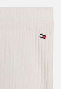 Tessuto a maglia crema a coste con un piccolo logo del marchio ricamato in rosso, bianco e blu sul lato.