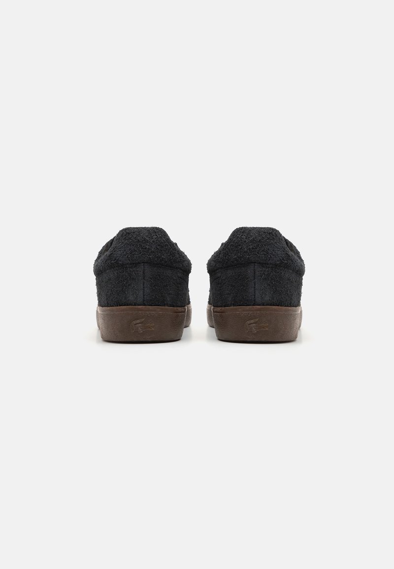 Pantofole nere pelose con una parte superiore testurizzata, schienale arrotondato e suole in gomma marrone. Il design presenta un branding minimale sul tallone.