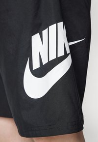 Black athletic shorts featuring a large white Nike logo. Made of smooth fabric with a modern cut and reinforced stitching at the hem.