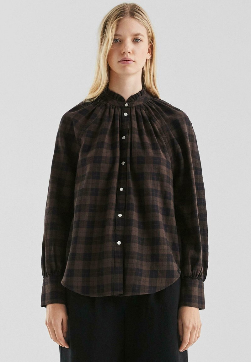Bruine geruite blouse met hoge hals, geplooide details en knoopsluiting. Lange mouwen met knoopmanchetten, gemaakt van een lichtgewicht stof.