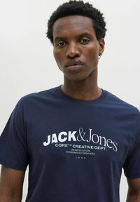 Mørkeblå bomulds t-shirt med et stort hvidt printdesign med "JACK & Jones" og yderligere tekst. Rundet halsudskæring og korte ærmer.