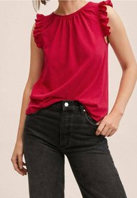 Rode mouwloze top met rimpelige schouders, geplooide halslijn en een zachte textuur, gecombineerd met hoge zwarte jeans met een knoopsluiting.