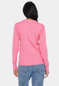 Rozā adīta džemperis ar garām piedurknēm, ribinātu apakšu un pūkainām plecu detaļām, apvienots ar augsta jostasvietas ziliem denim džinsiem.