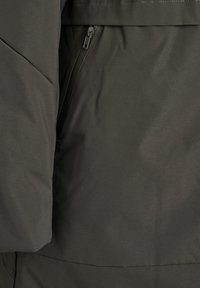 Primo piano di giacca in tessuto grigio scuro con linee di cucitura visibili e una tasca verticale sottile con zip.