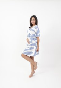 Vestido azul claro y blanco con patrones en forma de olas abstractas, mangas cortas, cintura ajustada y falda fluida. Sandalias de tacón cuadrado transparentes.
