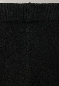 Gros plan d'un tissu noir tricoté avec une ceinture côtelée et un matériau doux et texturé en dessous.