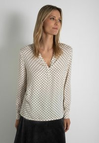 Crème blouse met zwarte stippen, v-hals, lange mouwen en een gladde stof; gecombineerd met een donkere corduroy rok.