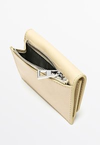 Portefeuille en cuir beige avec une finition texturée, doté d'une fermeture éclair argentée avec une languette rectangulaire et d'un intérieur noir contrastant.