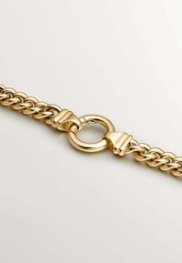 Pulsera de cadena de oro con eslabones entrelazados, una textura suave y un detalle de cierre redondo, todo ello sobre un fondo neutro.