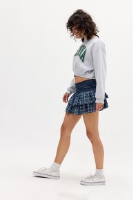 Grey cropped sweatshirt with "WINA" text, paired with a navy plaid pleated mini skirt. Model wearing white sneakers and cream socks.