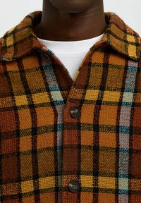 Bruine en oranje geruite blouse met zwarte en blauwe accenten, voorzien van een kraag, twee knopen en een gestructureerde stof.