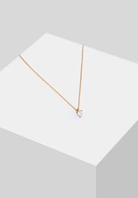 Gouden ketting met een delicate hartvormige hanger met een heldere edelsteen, die een strakke, minimalistische uitstraling heeft.