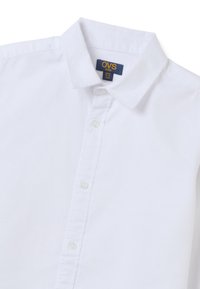 Witte kortebloezershirt van katoen met een kraag, knoopsluiting en een label met "OVS kids" op een blauwe achtergrond.
