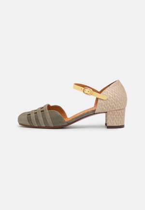 Zielone zamszowe buty na obcasie z żółtym paskiem na kostkę, z wycięciami z przodu i teksturowanym beżowym obcasem o geometrycznym wzorze.