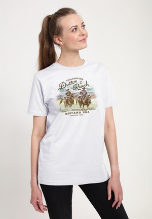 Femme avec une queue de cheval portant un T-shirt blanc avec deux cow-boys à cheval et le texte « Yellowstone Dutton Ranch Montana USA ».