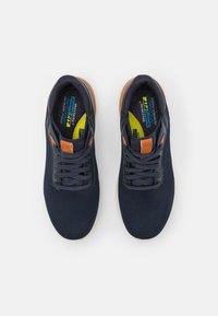 Zapatillas deportivas navy con parte superior de malla, detalles en naranja y cordones negros. Plantillas acolchadas visibles, con etiquetas amarillas y azules en el interior.