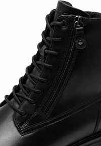 Botte cheville en cuir noir avec une finition lisse, équipée d'une fermeture éclair sur le côté, de lacets texturés et de coutures renforcées le long des bords.