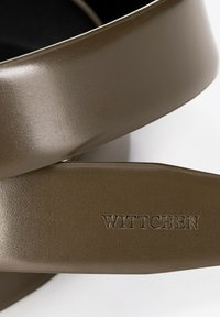 Bruine faux leren riem met een gladde, glanzende textuur. Voorzien van een gegraveerd logo "WITTCHEN" op de band, dat een stijlvolle uitstraling heeft.