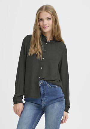 Blouse longue à manches longues vert foncé avec un col à volants, des boutons sur le devant et des manches à poignet, associé à un jean bleu taille haute.