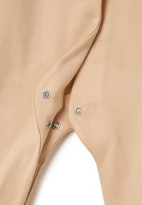 Tessuto di cotone beige con bottoni automatici sul lato, texture liscia e design leggermente elasticizzato, mostrando i dettagli delle cuciture e delle minuterie.