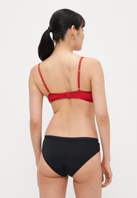 Raudonas liemenėlė su reguliuojamomis petnešėlėmis ir kabliukų užsegimu, derinama su juodomis trumpikėmis, kurių kraštai iškirpti banguotai. Lygios tekstūros, prigludusio dizaino.