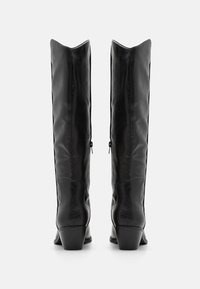 Des bottes noires en cuir montantes, au design épuré, avec des bouts pointus, des zips latéraux et un talon bas et large pour plus de stabilité. Texture lisse.