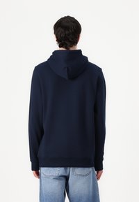 Felpa blu navy con una texture morbida, presenta un ampio cappuccio, maniche lunghe e orlo a coste. Indossata con jeans di denim blu chiaro.