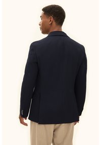 Marinblå blazer med strukturerade axlar, enda slits och två framfickor. Har knäppta manschetter och en slät tygstruktur.