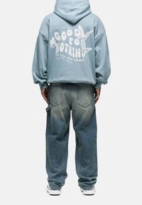 Sudadera azul recortada con texto blanco y gráfico de mariposa en la espalda, combinada con jeans de mezclilla sueltos y desgastados y zapatillas blancas.