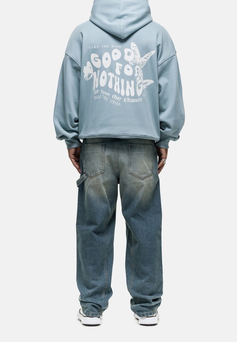 Sudadera azul recortada con texto blanco y gráfico de mariposa en la espalda, combinada con jeans de mezclilla sueltos y desgastados y zapatillas blancas.