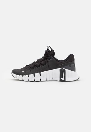Baskets athlétiques noir et blanc avec semelle texturée, design à lacets et logo de la marque sur le talon sur un fond clair uni.