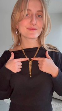 Collier en chaîne dorée composé de plusieurs maillons entrelacés, présenté en évidence sur un pull noir. Comprend un détail de fermoir au centre.