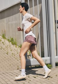 Running shoes in light beige, paired with white socks. The outfit includes a fitted white t-shirt and loose, light purple shorts.
