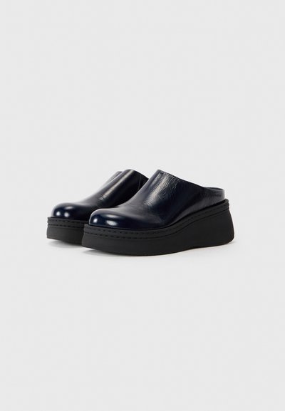 Chaussures en cuir bleu marine à enfiler avec un bout arrondi et une semelle plateforme noire épaisse. La tige présente une texture lisse avec des détails de couture visibles.