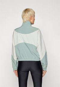Chaqueta ligera en verde menta y blanco, con un alto cuello, cinturilla elástica y un ajuste relajado con hombros caídos.