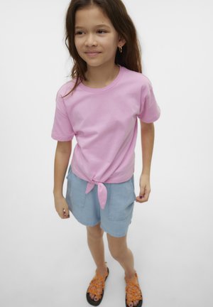 Roze katoenen T-shirt met een geknoopte voorkant, gecombineerd met lichtblauwe denim shorts en oranje sandaaltjes met bandjes. Eenvoudig ontwerp, casual pasvorm.