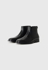 Botas de tobillo de cuero negro con una textura suave, puntera redondeada, cremallera lateral y tacón bajo apilado. Diseño clásico adecuado para varios conjuntos.