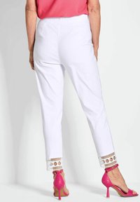 Witte broek met decoratieve kanten rand bij de broekspijpen, gecombineerd met roze hoge hakken. Glad materiaal met een getailleerde pasvorm.