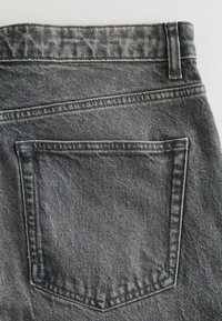 Tylnia kieszeń wyblakłych czarnych dżinsów z widocznym przeszyciem i pętlą na pasek na białym tle.