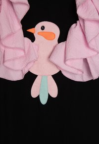 Vêtement noir avec un col froncé rose. Applique centrale représentant un oiseau avec un corps rose, un bec orange et une queue verte. Tissu texturé.