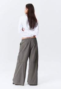 Pantalon à jambes larges en mélange de coton vert olive, avec une taille élastique, une coupe décontractée et des coutures apparentes.